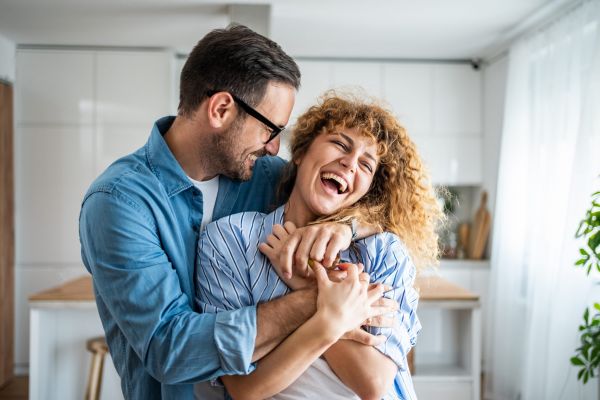 A couple laughing and embracing in a bright kitchen setting.