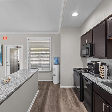 Modern kitchen in community center at Encino Park Apartments with dark cabinets, granite countertops, and stainless steel appliances. Bright overhead lighting.